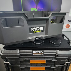 May include: Two stacked toolboxes. The top toolbox is gray with the "RYOBI LINK" logo. The bottom toolbox is black with the "RIDGID PRO GEAR SYSTEM GEN 2.0" logo and orange accents. The toolboxes are designed for tool storage.