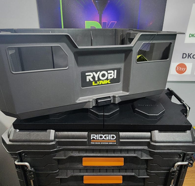 May include: Two stacked toolboxes. The top toolbox is gray with the "RYOBI LINK" logo. The bottom toolbox is black with the "RIDGID PRO GEAR SYSTEM GEN 2.0" logo and orange accents. The toolboxes are designed for tool storage.