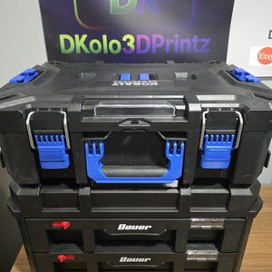 May include: Black and blue tool storage system with the brand name "KOBALT" and "Bauer" visible. The system includes a top storage box with blue accents and metal latches, stacked on top of two drawers. The top box has a clear plastic handle.