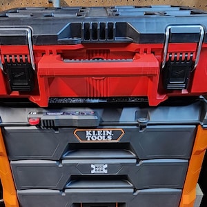 May include: Two stacked toolboxes. The top toolbox is red and black with metal latches and a handle. The bottom toolbox is gray and orange with the Klein Tools logo and Mod Box text.
