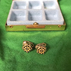 May include: A gold metal jewelry box with a mirror and eight compartments. The box is open and there are two gold earrings with black and gold designs inside.