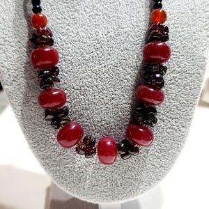 May include: A red and black beaded necklace with a variety of red and black beads. The necklace is on a gray mannequin.