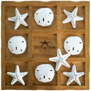 May include: A wooden game board with nine compartments, each containing a white sand dollar or a white starfish. The board has the text "Nautical Crush Trading" printed on it.