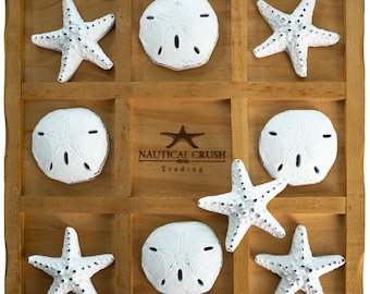 May include: A wooden game board with nine compartments, each containing a white sand dollar or a white starfish. The board has the text "Nautical Crush Trading" printed on it.