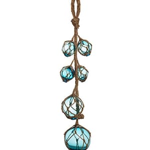 May include: A decorative hanging ornament featuring six blue glass spheres encased in woven netting. The spheres are suspended from a brown rope, creating a nautical or coastal theme. The ornament is designed for hanging.