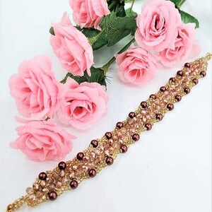 May include: A beaded bracelet featuring a woven pattern of light pink faceted crystals and small dark brown spherical beads, accented with gold-toned seed beads. The bracelet includes a gold-toned lobster claw clasp at one end for closure.