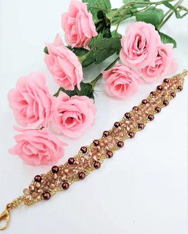 May include: A beaded bracelet featuring a woven pattern of light pink faceted crystals and small dark brown spherical beads, accented with gold-toned seed beads. The bracelet includes a gold-toned lobster claw clasp at one end for closure.