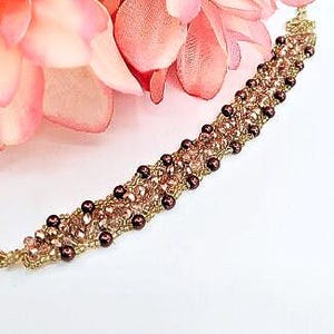 May include: A beaded bracelet featuring a woven design of metallic gold thread, small dark brown spherical beads, and light pink faceted crystals. The bracelet includes a gold-toned lobster claw clasp at one end for secure fastening.
