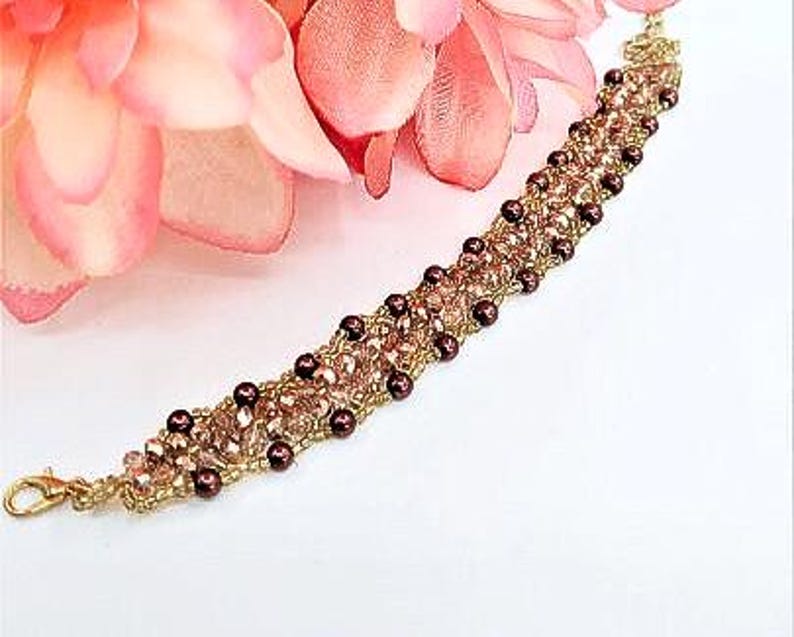 May include: A beaded bracelet featuring a woven design of metallic gold thread, small dark brown spherical beads, and light pink faceted crystals. The bracelet includes a gold-toned lobster claw clasp at one end for secure fastening.