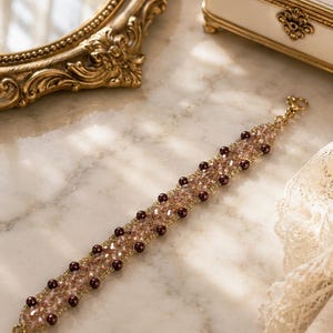 May include: A beaded bracelet featuring a central band of shimmering light brown faceted crystals flanked by two rows of small, dark brown spherical beads. The bracelet is finished with a gold-toned metal lobster claw clasp at each end.