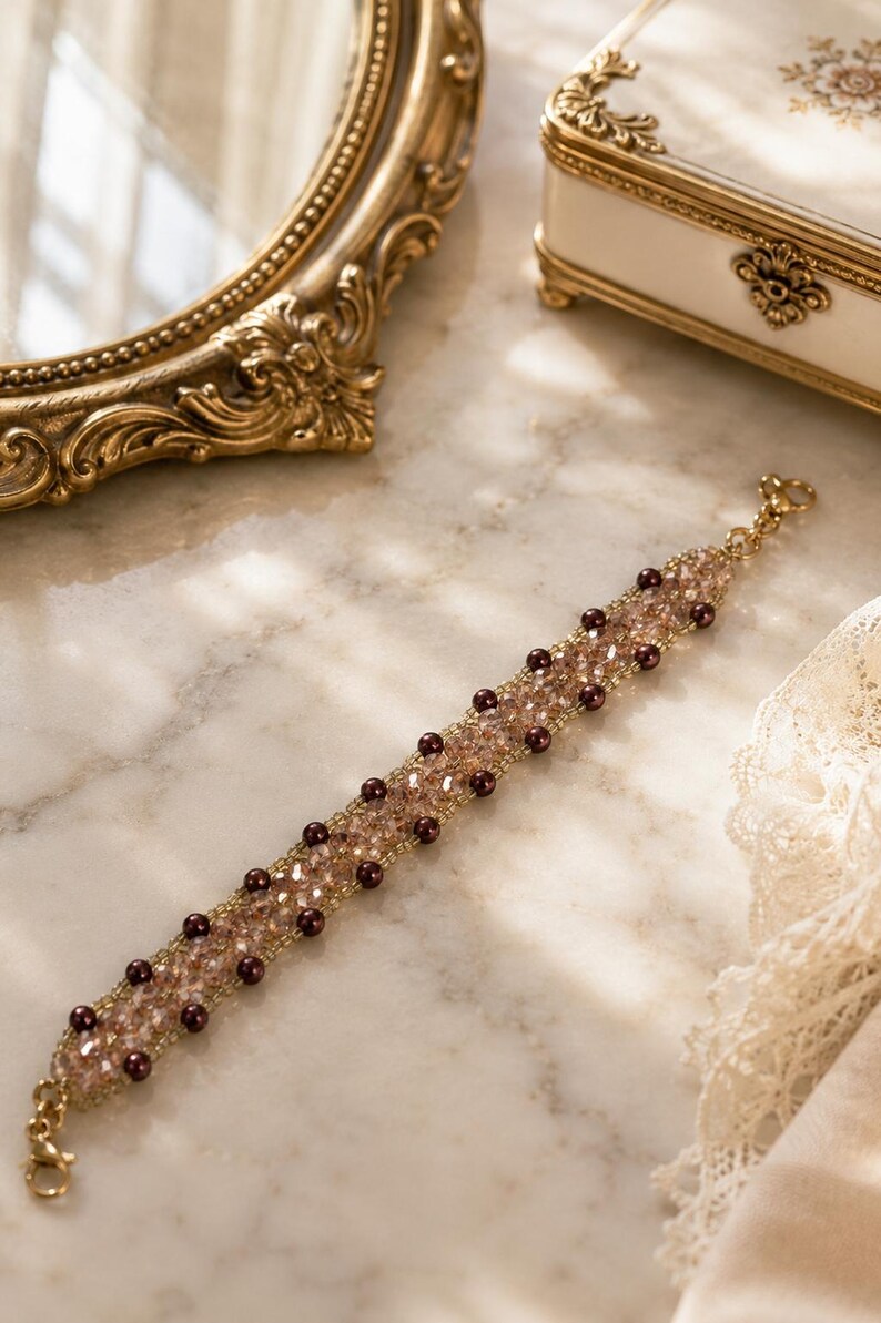 May include: A beaded bracelet featuring a central band of shimmering light brown faceted crystals flanked by two rows of small, dark brown spherical beads. The bracelet is finished with a gold-toned metal lobster claw clasp at each end.