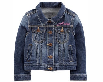 Könnte beinhalten: Eine blaue Jeansjacke mit einem rosa gestickten Namen "Andrea" auf der Brust.