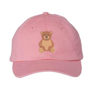 May include: Pink baseball cap with an embroidered brown teddy bear sitting on the front.