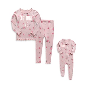 May include: Pink pajamas with a floral print. The top has the text "CUSTOMIZE ME" on it. The bottom is a pair of pants. The second pajama set is a pink one-piece with the text "NAME" on it.