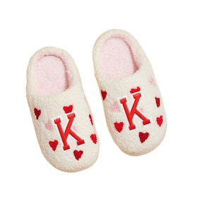 May include: A pair of white fuzzy slippers with red hearts and the letter "K" embroidered on them.