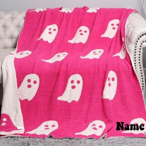 K&ouml;nnte beinhalten: Eine rosa Kuscheldecke mit einem wei&szlig;en Geistermuster. Die Decke ist gefaltet und auf einem wei&szlig;en Sofa drapiert. Der Text "Name" ist in der unteren rechten Ecke des Bildes sichtbar.