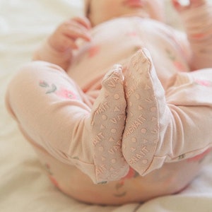 May include: A pink baby onesie with a floral pattern and grippy feet. The onesie is made of soft, breathable fabric and is perfect for keeping baby warm and comfortable.
