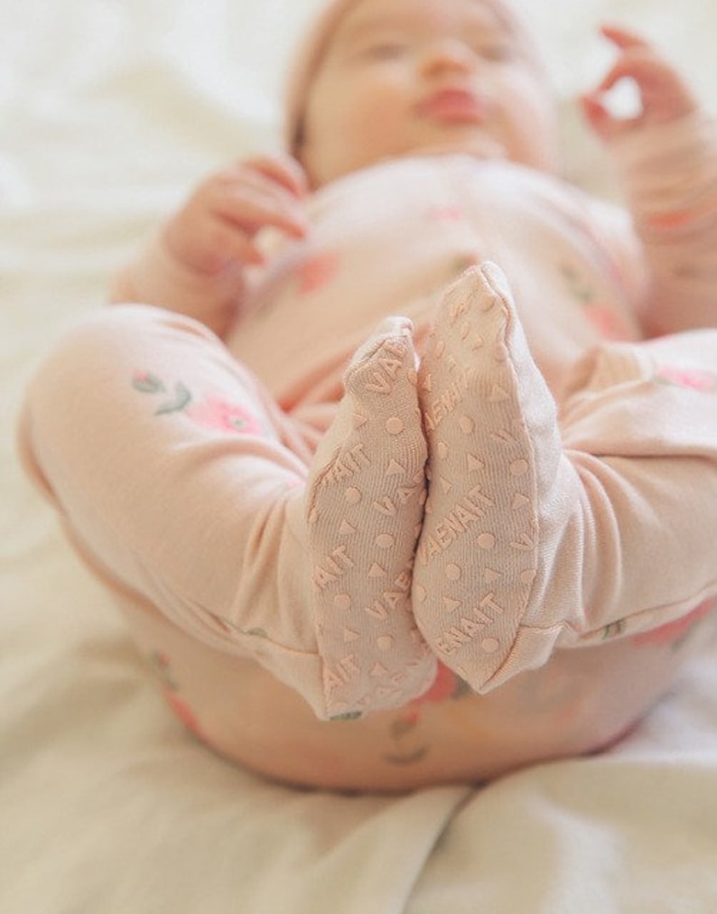 May include: A pink baby onesie with a floral pattern and grippy feet. The onesie is made of soft, breathable fabric and is perfect for keeping baby warm and comfortable.