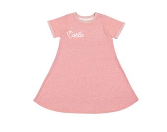 以下が含まれることがあります： 「Carla」という名前が前面に刺繍された、ピンクの半袖Tシャツドレスです。