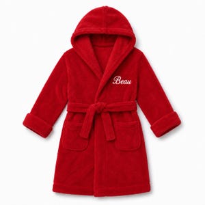 May include: A bright red plush hooded bathrobe featuring long sleeves, two front patch pockets, and a matching tie belt at the waist. The name Beau is embroidered in white cursive script on the upper left chest area of the robe.