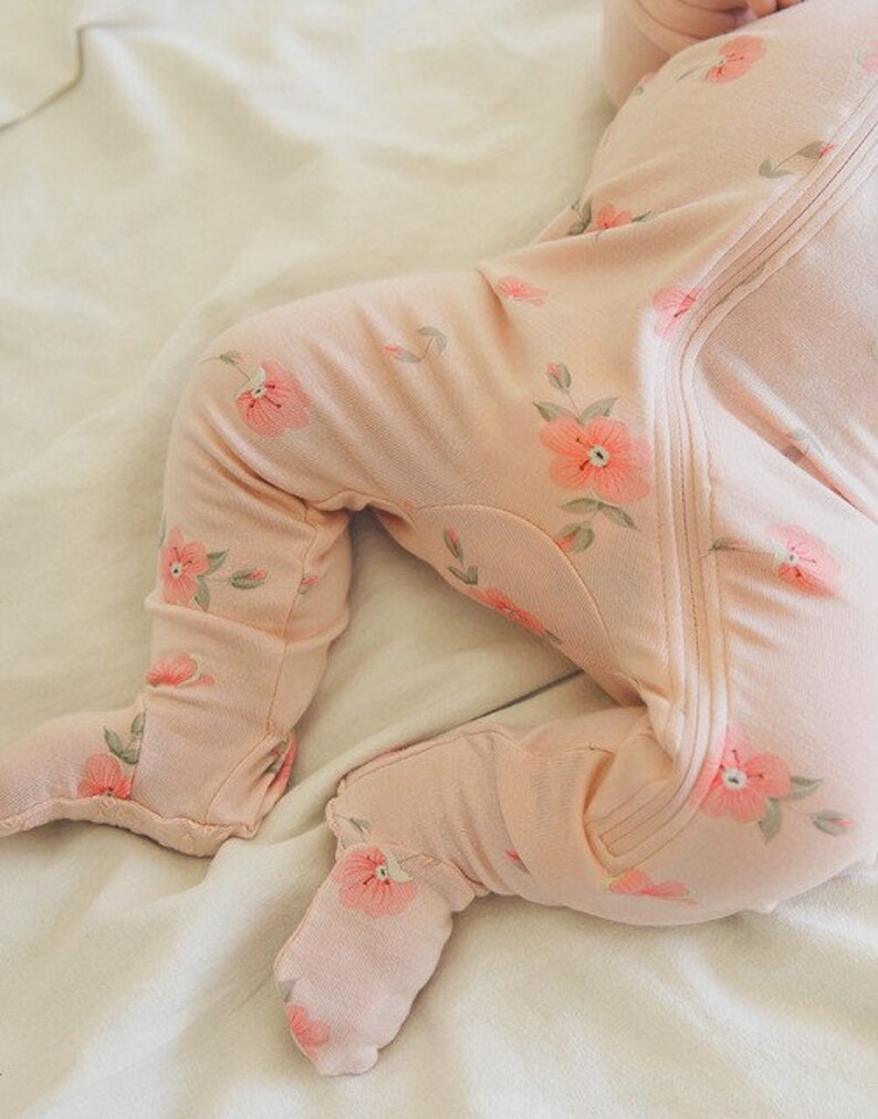 May include: A pink baby sleeper with a floral print. The sleeper has a zipper down the front and footie feet.