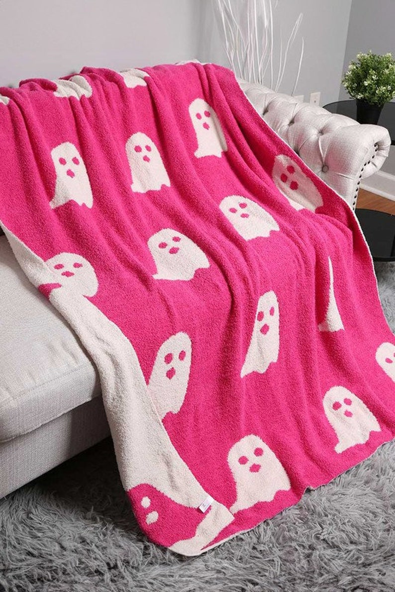 K&ouml;nnte beinhalten: Eine rosa Kuscheldecke mit einem wei&szlig;en Geistermuster. Die Decke ist weich und flauschig, perfekt zum Kuscheln auf der Couch.