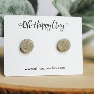 May include: A pair of small, round, speckled gray clay earrings on a white card with the text "Oh Happy Clay" and "www.ohhappyclay.com".