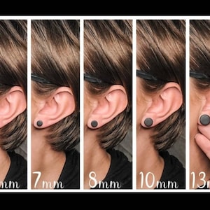 Puede incluir: Una serie de cinco pendientes de bot&oacute;n circulares negros mostrados en l&oacute;bulos de oreja, etiquetados con los tama&ntilde;os 6mm, 7mm, 8mm, 10mm y 13mm. Cada pendiente es un disco negro s&oacute;lido y simple, que demuestra la diferencia de escala visual.