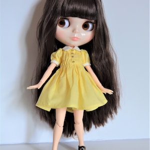 May include: A doll with long brown hair wearing a yellow dress and black shoes.