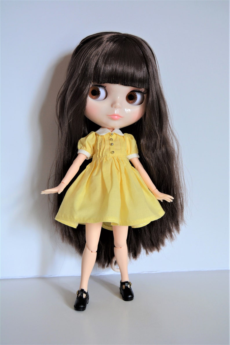 May include: A doll with long brown hair wearing a yellow dress and black shoes.