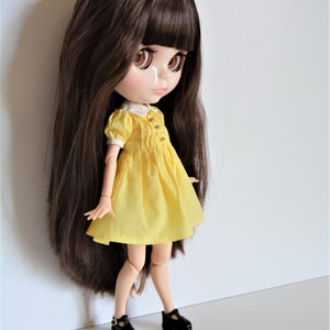 May include: A doll with long brown hair wearing a yellow dress and black shoes.