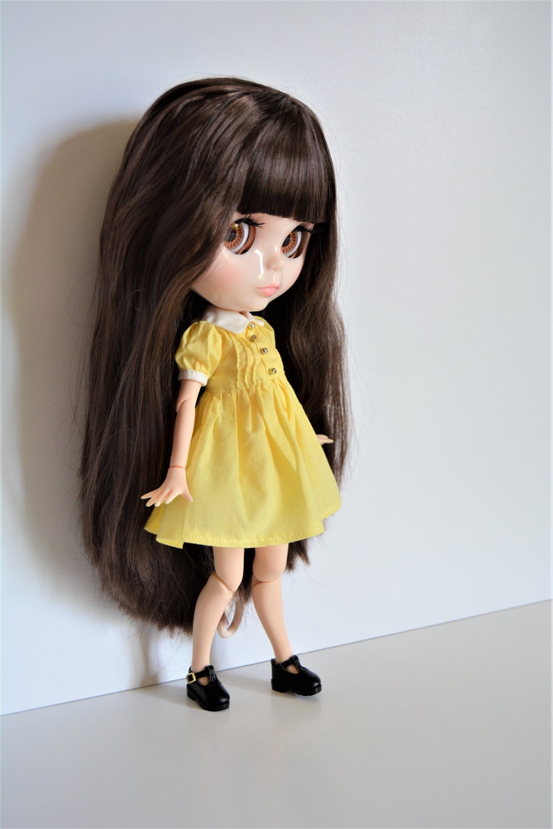 May include: A doll with long brown hair wearing a yellow dress and black shoes.