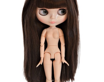 May include: A doll with long, dark brown hair and large, expressive eyes. The doll has a neutral skin tone and articulated joints. It is a collectible doll, likely for display or play.
