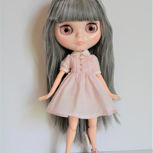 May include: A doll with long gray hair, wearing a pink dress with a white collar and pink shoes.