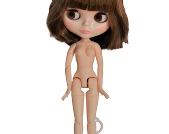 May include: A nude doll with brown hair and brown eyes. The doll has a bob haircut with bangs. The doll is standing with its arms outstretched.