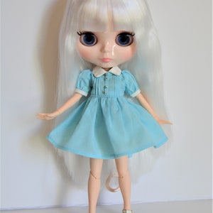 May include: A white doll with long, straight, white hair wearing a light blue dress with a white collar and white shoes.