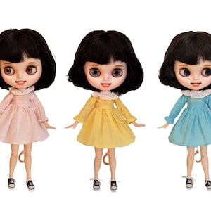 Puede incluir: Tres mu&ntilde;ecas con cabello negro y flequillo que llevan vestidos de diferentes colores. Las mu&ntilde;ecas llevan cuellos de encaje blanco y zapatos negros. Los vestidos son rosa, amarillo y azul.