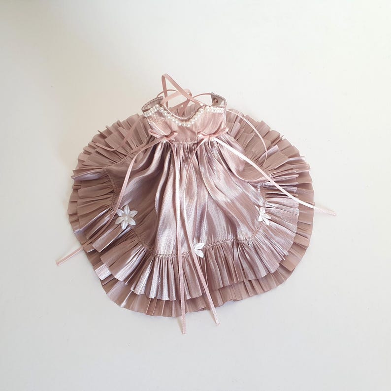 K&ouml;nnte beinhalten: Ein rosa Satin-Kleid mit wei&szlig;en Blumenverzierungen und einem R&uuml;schenrock.