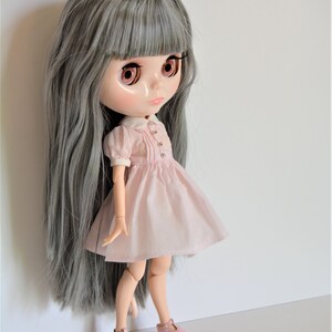 May include: A doll with long gray hair, wearing a pink dress with a white collar and pink shoes.