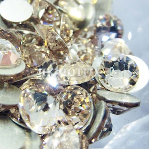 Puede incluir: Primer plano de un montón de pequeños diamantes de imitación transparentes y facetados de color marrón claro ámbar. Los diamantes de imitación están dispuestos en un patrón aleatorio y reflejan la luz.