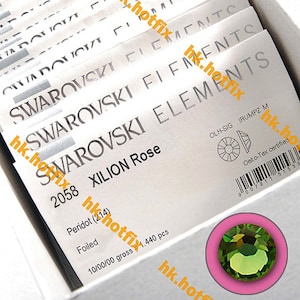May include: A close-up of a package of Swarovski Xilion Rose Peridot crystals. The package is white with black text and a barcode. The crystals are green and have a foiled finish. The package says "10/00/00 gross 1,440 pcs".