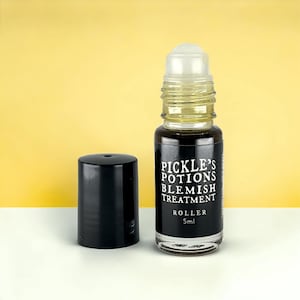 Puede incluir: Un pequeño frasco de vidrio con rodillo y una etiqueta negra que dice "Pickle's Potions Blemish Treatment". El frasco contiene un líquido oscuro y tiene un aplicador de bola transparente. Una tapa negra está al lado del frasco. El frasco es de 5 ml.