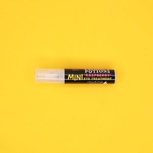 Op de afbeelding: Een klein, doorzichtig plastic flesje met een zwart etiket waarop "FAIRY'S POTIONS MINI 'RASPBERRY' EYE TREATMENT routine 6" en "3ml." staat.