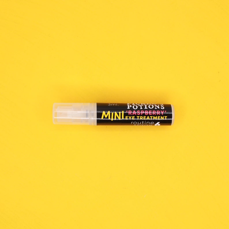 Op de afbeelding: Een klein, doorzichtig plastic flesje met een zwart etiket waarop "FAIRY'S POTIONS MINI 'RASPBERRY' EYE TREATMENT routine 6" en "3ml." staat.