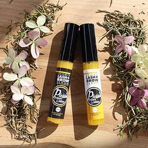 K&ouml;nnte beinhalten: Zwei gelb-schwarze Flaschen Wimpern- und Augenbrauenserum mit dem Text "Grow Lash + Brow Serum" und "Vital Lash + Brow Serum". Die Flaschen sind von Rosmarinzweigen und kleinen rosa und wei&szlig;en Bl&uuml;ten umgeben. Der Text "Pickles & Botanicals" ist ebenfalls sichtbar.