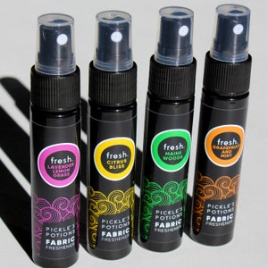 Puede incluir: Cuatro peque&ntilde;os frascos pulverizadores negros con etiquetas de diferentes colores. Cada etiqueta tiene la palabra "fresh." y un nombre de aroma diferente. Las etiquetas tambi&eacute;n dicen "Pickle's Potions Fabric Freshener".