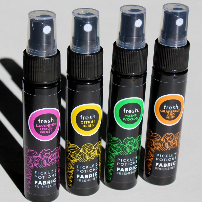 Puede incluir: Cuatro peque&ntilde;os frascos pulverizadores negros con etiquetas de diferentes colores. Cada etiqueta tiene la palabra "fresh." y un nombre de aroma diferente. Las etiquetas tambi&eacute;n dicen "Pickle's Potions Fabric Freshener".