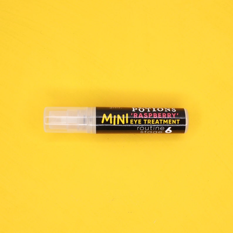 Op de afbeelding: Een klein, doorzichtig flesje met een zwart etiket waarop "POTIONS 'RASPBERRY' EYE TREATMENT routine stage 6" staat op een gele achtergrond.