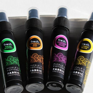 Puede incluir: Cuatro peque&ntilde;os frascos pulverizadores negros con etiquetas de diferentes colores. Cada etiqueta tiene la palabra "fresh." y un aroma diferente: Bosques de Maine, Pomelo y Menta, Lavanda Hierba Lim&oacute;n, y Felicidad C&iacute;trica. Cada frasco dice "Pickle's Potions Suavizante de Tela."