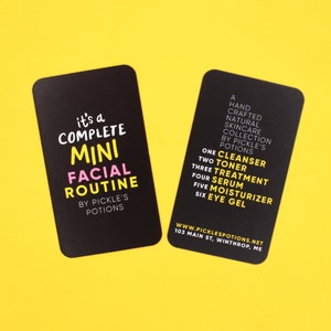 Op de afbeelding: Twee zwarte kaarten met witte tekst. De kaart links zegt "it's a COMPLETE MINI FACIAL ROUTINE BY PICKLE'S POTIONS". De kaart rechts somt de stappen op in een huidverzorgingsroutine: "ONE CLEANSER, TWO TONER, THREE TREATMENT, FOUR SERUM, FIVE MOISTURIZER, SIX EYE GEL". De kaart bevat ook het websiteadres "WWW.PICKLESPOTIONS.NET" en het adres "103 MAIN ST, WINTHROP, ME".
